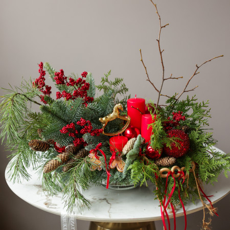 Композиция из живой хвои с красными свечами и золотой лошадкой-качалкой