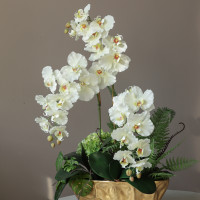 Композиция с белыми орхидеями и декоративной зеленью в дизайнерской золотой вазе 