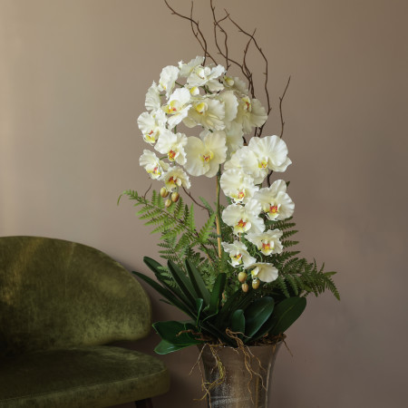 Напольная композиция с молочными орхидеями, зеленью и декоративными веточками в высокой металлической вазе на ножке